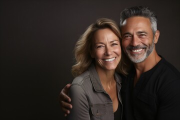 middle aged couple smiling on dark brown background