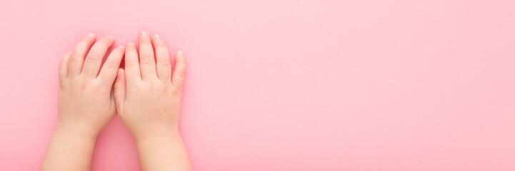 Little girl hands on light pink table background. Pastel color. Closeup. Point of view shot. Wide banner. Empty place for text. Top down view.
