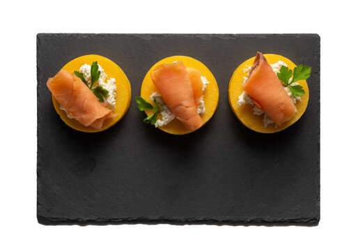 Black slate tray with three portions of polenta with salmon and cheese
