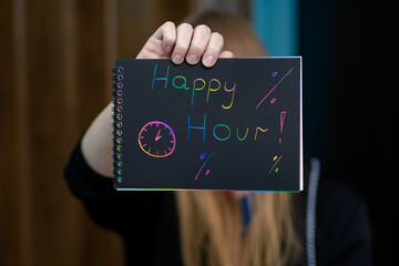 Kobieta trzyma w dłoniach reklamę infkrmujaca o happy hour, napis na kartce