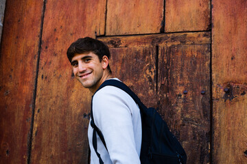 young pleased man smiling at the camera in front of an ancient door, open gesture