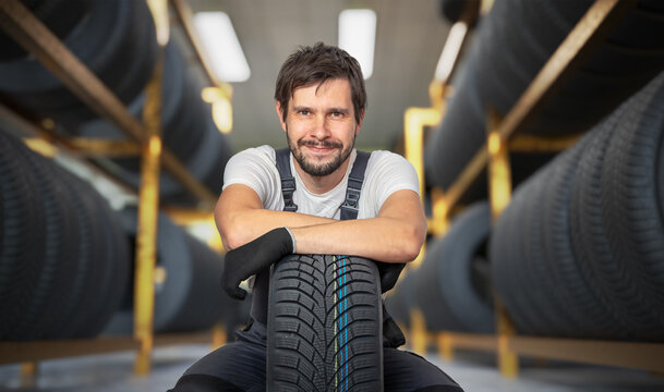 Happy car mechanic with tire in tire store.