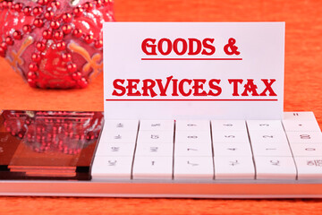 Goods and services and tax text written on a white business card on a calculator on an orange background