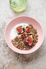 Roseate bowl with granola, greek yogurt and fresh figs, vertical shot on a beige granite background, elevated view