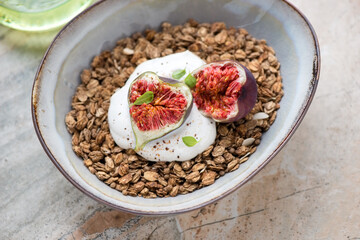 Bowl of granola served with torn fig fruits and greek yogurt, horizontal shot on a beige granite surface, middle close-up