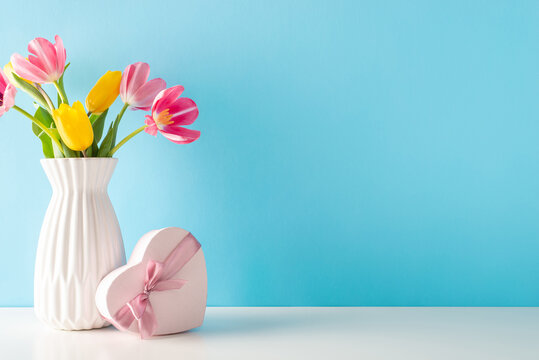 Mother's Day and 8 March theme: side view table features a heart-shaped present and a vase of vibrant tulips against a soft blue backdrop, offering blank space for your message