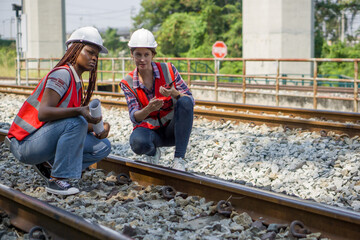 Rail transportation engineer in safety vest and hardhat check the neatness of the railway track while holding walkie-talkie and train route chart.