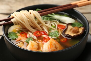Bowl of delicious ramen with chopsticks on table, closeup. Noodle soup