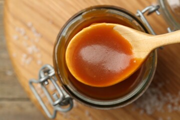 Jar and spoon with tasty salted caramel on table, top view