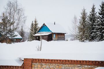 Small wooden house with blue roof in winter forest on snowy field near brick wall fence - Powered by Adobe