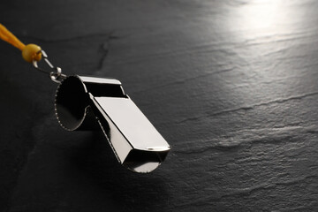 Referee equipment. Metal whistle on black textured background, closeup and space for text