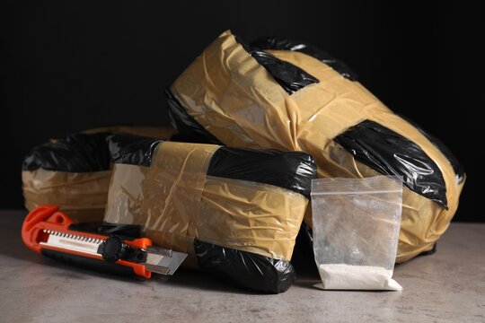Smuggling, drug trafficking. Packages with narcotics and utility knife on grey table