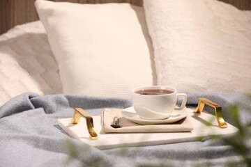 Aromatic tea in cup, saucer and spoon on bed