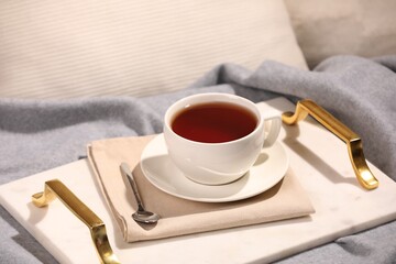 Aromatic tea in cup, saucer and spoon on bed