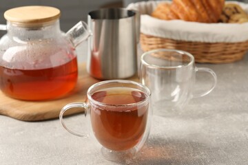 Aromatic tea in glass cup and teapot on light grey table