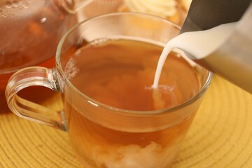 Pouring milk in tea at table, closeup