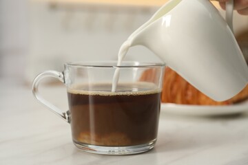 Pouring milk in coffee at white table, closeup