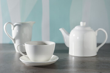 Aromatic tea in teapot, cup and pitcher on gray table against color background