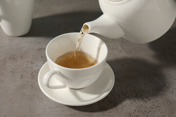 Pouring aromatic tea in cup at gray table, closeup