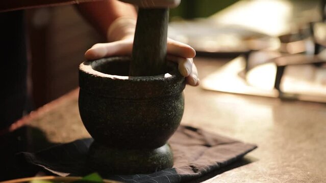 Chef is pounding chilli paste from herbs and spice in the kitchen