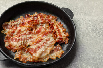 Delicious bacon slices in frying pan on grey table, closeup