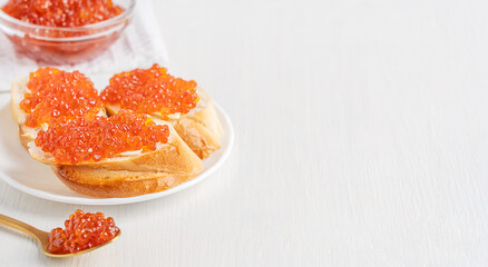 Three slices of loaf of bread or canape with butter and salted salmon fish roe or red caviar served on plate with spoon and glass bowl on white wooden background with copy space as healthy snack