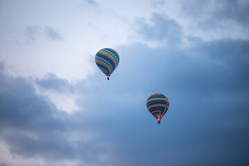 Montgolfières colorées en ascension dans un ciel nuageux - obrazy, fototapety, plakaty