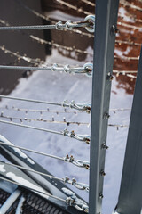 Close-up of a metal railing with cable wires against a snowy background.
