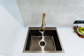 Single-bowl stainless steel kitchen sink with a modern gold faucet. Isolated on a white background.