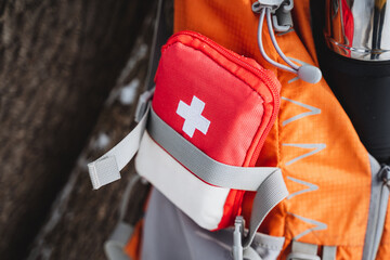 Red and white first aid kit attached to backpack, ideal for travel, hiking, camping.