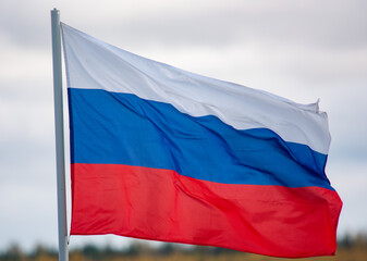 The white-blue-red flag of the Russian Federation is flying in the wind against a cloudy sky.