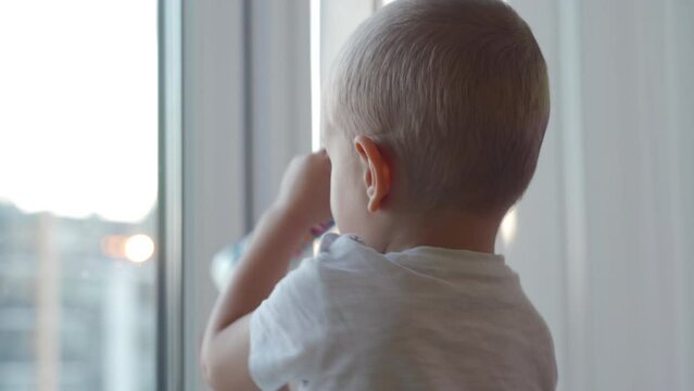 3-year-old child sitting by the window in winter, little boy looks out the window onto the street.