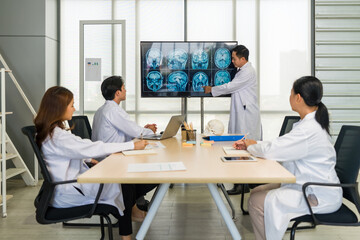 Group of doctor in white gown, discussing brain scans on large monitor in a meeting room.
