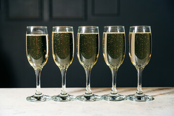 Five sparkling champagne glasses lined up on a table, with bubbles rising to the surface, ready for a toast.