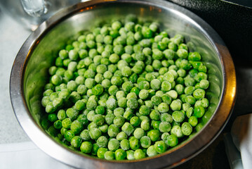 Frozen Green Peas in Stainless Steel Bowl. A bowl full of frozen green peas with frost, showcasing the raw and healthy ingredient for cooking.
