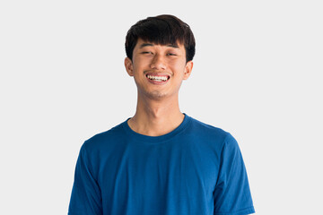 Young Asian man in blue t-shirt smiling happily isolated on gray background. The concept of being...