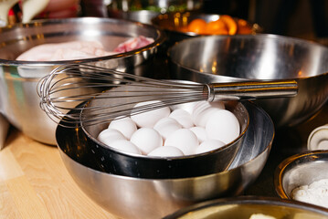 Whole Eggs and Whisk in Kitchen Bowls. A bowl full of whole eggs next to a stainless steel whisk, ready for baking or cooking in a home kitchen.