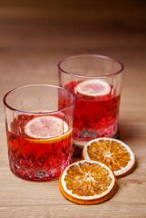 Two glasses of red cocktail with ice and lemon slices on wooden background vertical copy space