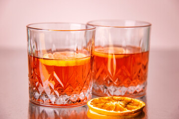 Two glasses of brandy with lemon and slices of orange on a pink reflection background with copy space