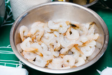 Fresh Raw Shrimp in a Metal Bowl Ready for Cooking. A bowl of fresh, uncooked shrimp with tails, prepared for culinary use, displayed on a kitchen countertop.