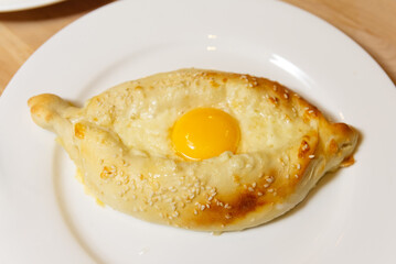 Baked Pastry with Egg and Sesame Seeds. A freshly baked pastry filled with cheese, topped with a sunny-side-up egg and sprinkled with sesame seeds on a white plate.