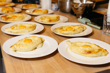 Baked Adjarian Khachapuri with Egg on Top. Multiple servings of Adjarian khachapuri, a traditional Georgian cheese bread with a sunny-side up egg, freshly baked and served on white plates.