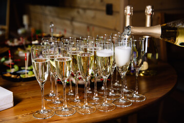 Champagne Service at a Cozy Event Gathering. A close-up view of champagne being poured into flutes, ready for a toast at an intimate social event with appetizers in the background.