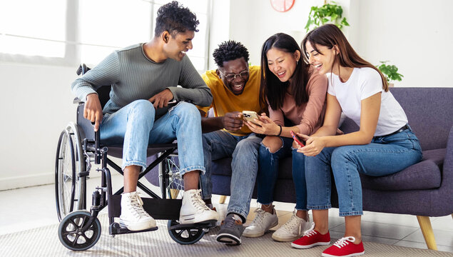 Man on wheelchair with friends having fun watching smart mobile phone device - Happy teenagers posting picture on social media - Youth lifestyle concept