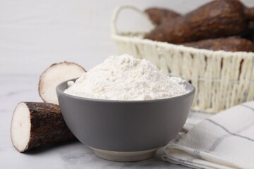 Bowl with cassava flour and roots on white marble table