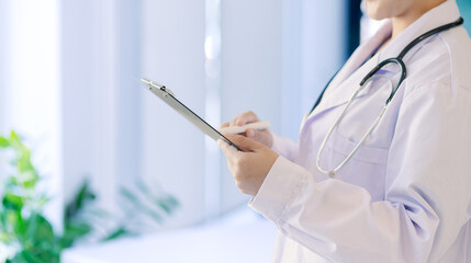 Asian female doctor holding a patient clipboard and standing at hospital, Healthcare and medical concept.