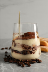 Tasty tiramisu in glass, coffee beans, spoon and biscuits on light grey table, closeup