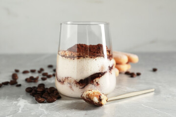 Tasty tiramisu in glass, coffee beans, spoon and biscuits on light grey table, closeup