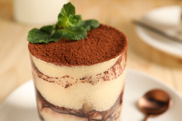 Tasty tiramisu and mint in glass on table, closeup