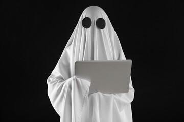 Creepy ghost. Person in white sheet with laptop on black background